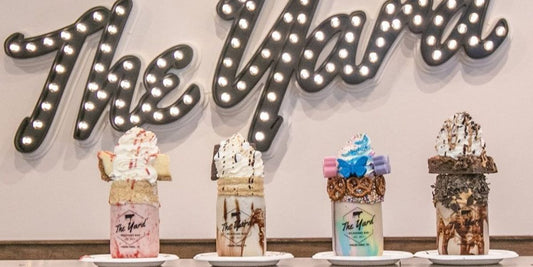 a row of mason jar milkshakes in front of the yard sign